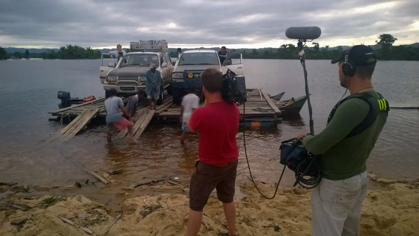 Équipe de tournage filmant des 4x4 chargés sur un bac en bois, sur une rivière à Madagascar