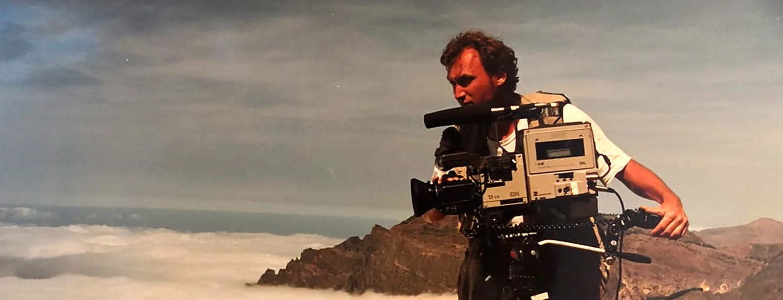 Camera operator with a classic broadcast camera on a tripod above a sea of clouds