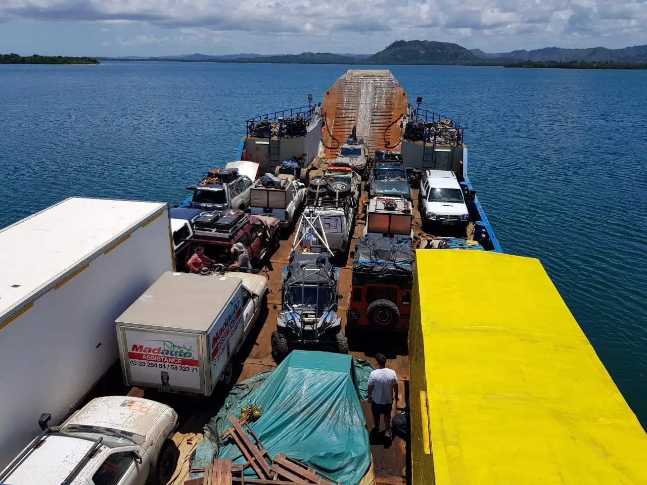 Convoi de véhicules de production et de camions traversant une baie sur une barge à Madagascar