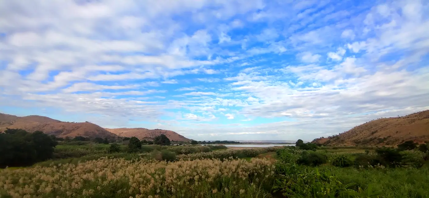 Wide view of hills, reed fields and a lake under a cloudy sky, Madagascar