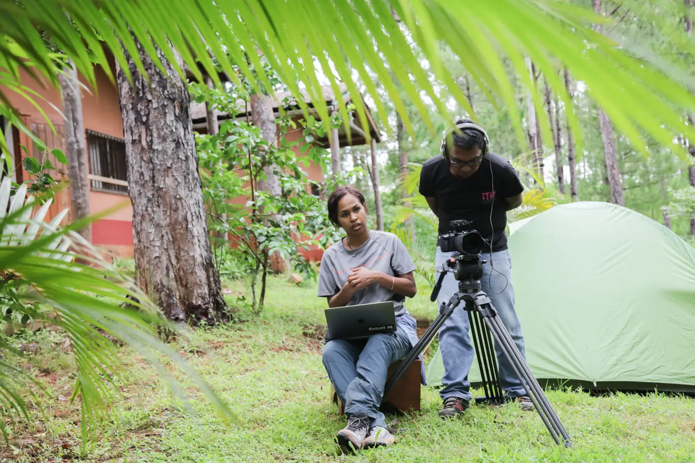 Director with a laptop and a camera operator filming in a pine forest camp in Madagascar