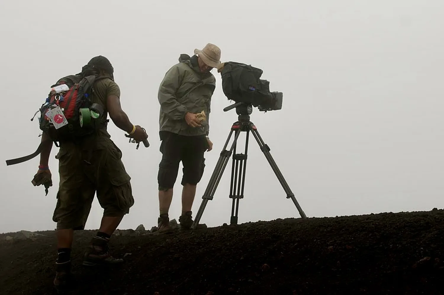 Two crew members setting up a camera on a tripod on a misty hillside in Madagascar
